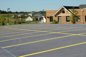 Freshly striped asphalt parking lot near a residential area, shown during spring with clear skies.